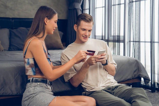Genç çift, kredi kartıyla ödemek için internet üzerinden ödeme uygulaması ve dijital cüzdan kullanarak yatak odasında oturuyor. Mobil internet üzerinden alışveriş ve modern alımlar. Açılıyor - Fotoğraf, Görsel