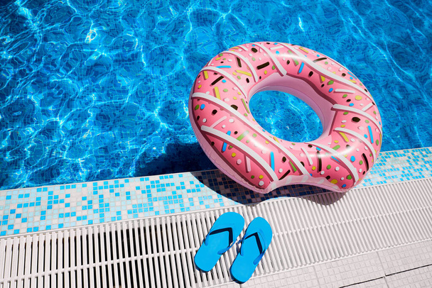 Różowy nadmuchiwany pierścień i niebieskie gumowe japonki wykonane z niebieskiej wody na zewnątrz basenu. Relaks przy basenie. - Zdjęcie, obraz