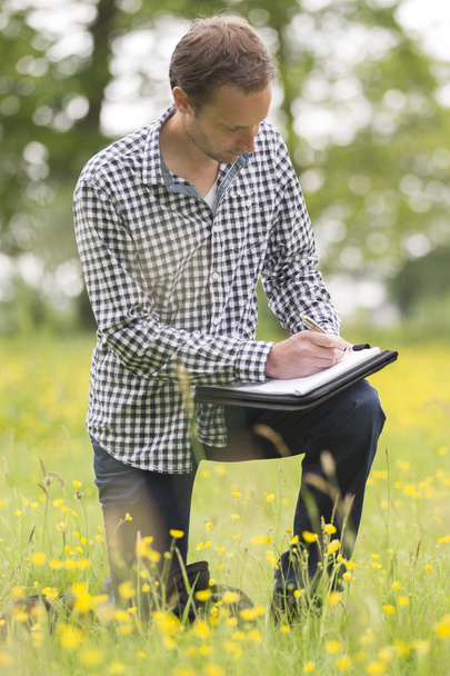 Environmentalist Writing On Notepad On Field - Foto, Imagen