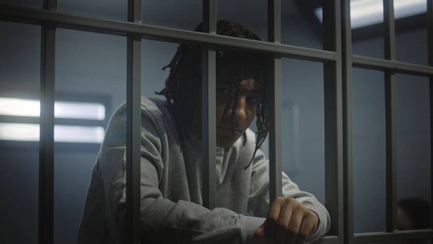 Depressieve Afro-Amerikaanse tiener met tatoeages staat in de gevangenis in de cel en kijkt naar camera. Jonge gevangene zit gevangenisstraf uit voor misdaad. Jeugddetentiecentrum of -gevangenis. - Foto, afbeelding