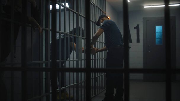 Warden brings new prisoner in jail cell and takes off his handcuffs. African American teen serves imprisonment term in correctional facility or detention center. Young inmates in jail. Tracking shot. - Photo, Image