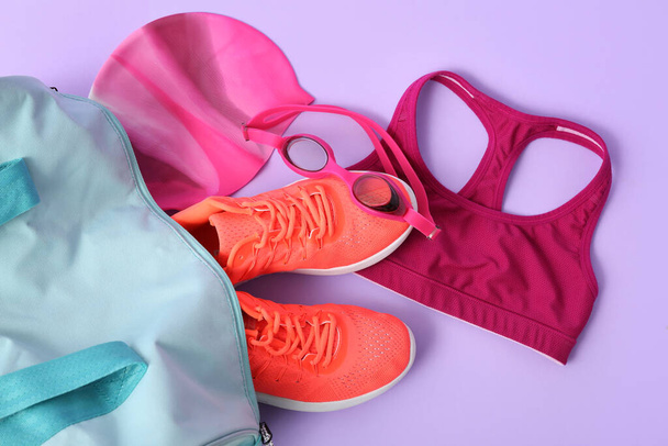 Sporttas met zwemuitrusting en bril op paarse achtergrond - Foto, afbeelding