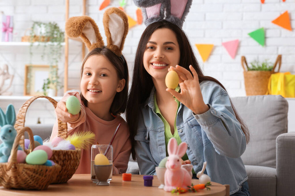 Маленька дівчинка і її мати у вухах кролика малюють великодні яйця у вітальні - Фото, зображення