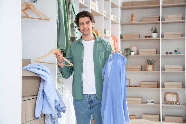 Красивый молодой счастливый человек с шкафом для одежды и стильной одеждой в гримерке - Фото, изображение