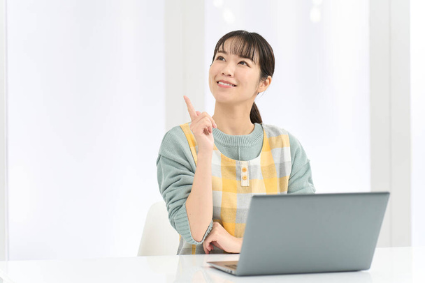 Uma mulher vestindo um avental vem com boas ideias enquanto trabalhava em um computador - Foto, Imagem