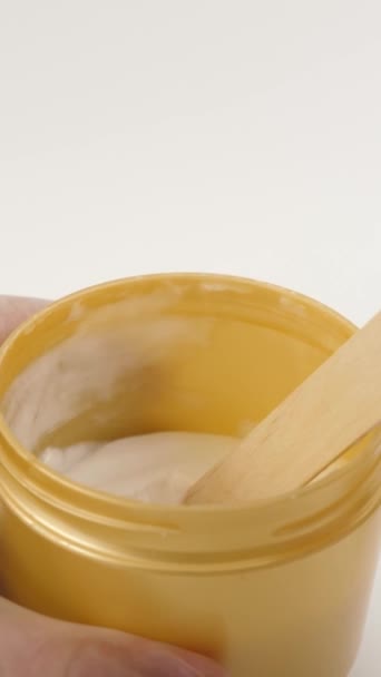 Ein kosmetisches Gel aus einem Plastikgefäß wird auf einen Holzspatel aufgetragen. Vertikales Video - Filmmaterial, Video