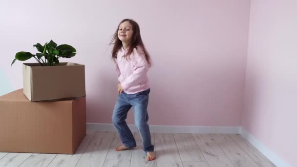 Mała dziewczynka szczęśliwie tańczy w pobliżu pudeł z rzeczami, radując się w swoim nowym domu. Nowa obudowa. Nieruchomości i dzierżawa, kredyt i hipoteka, koncepcja dzień przeprowadzki. Zwolniony ruch. - Materiał filmowy, wideo