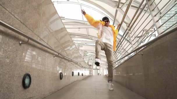 Taitava iloinen aasialainen hipsteri kävelee tanssiessaan kapealla käytävällä. Lähikuva tanssija harjoitellaan break dance esitystä. Ammattimies siirtymässä musiikkiin. Ulkoilu 2024. Sujuvasti.. - Materiaali, video