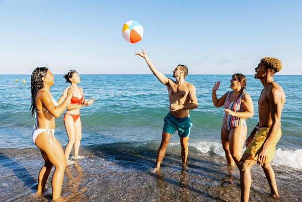 Joven grupo de amigos que se divierten jugando con la pelota de playa en el agua durante las vacaciones de verano - Foto, imagen