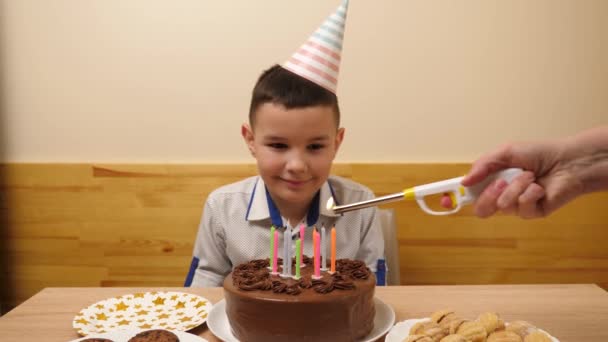 El tipo está sentado frente a una mesa con un pastel festivo en el que se encienden las velas. Concepto de celebración de cumpleaños. - Imágenes, Vídeo