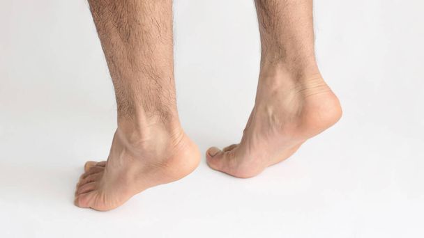 Zwei männliche Füße, die auf Zehenspitzen stehen und Spannungen in der Achillessehne zeigen, mit weißem Hintergrund - Foto, Bild