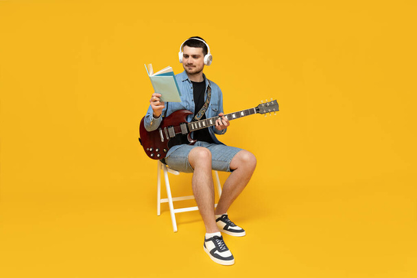 Attraente giovane ragazzo con una chitarra tra le mani su uno sfondo giallo - Foto, immagini