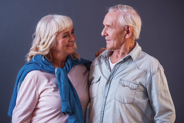 Velho bonito e mulher em roupas casuais estão olhando um para o outro e sorrindo, em fundo cinza
 - Foto, Imagem