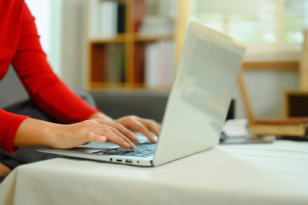 Закройте руки молодой женщины в красном свитере, печатая на клавиатуре ноутбука. - Фото, изображение