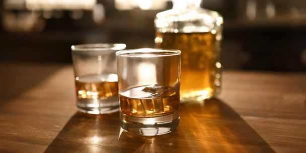Zaměřte se na dvě sklenice a láhev s whisky nebo bourbon na dřevěném stole. Luxusní drink s kostkami ledu na stole. Oslavný koncept. Rozmazané pozadí - Fotografie, Obrázek