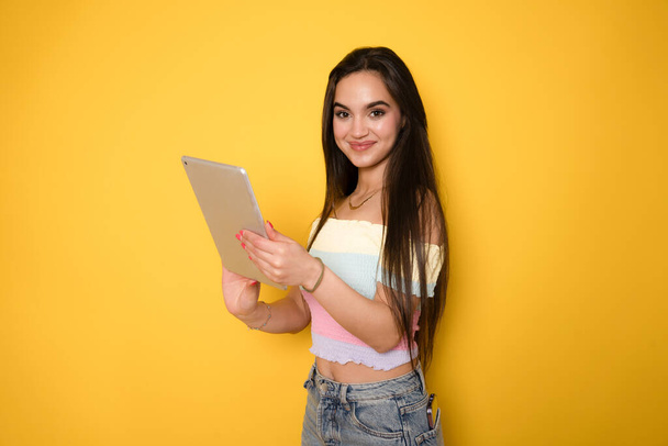 黄色の背景に隔離されたデジタルタブレットを使用してスマートなインテリジェントな白人ヒスパニックラテンアメリカの若い女性学生. - 写真・画像