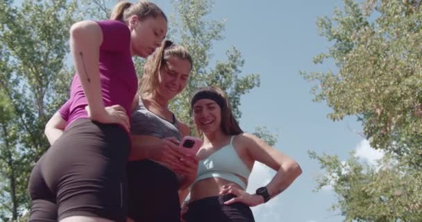Actieve vrouwelijke sportvrienden delen een lach en het controleren van een sociale media op een telefoon na het sporten in het park. - Video