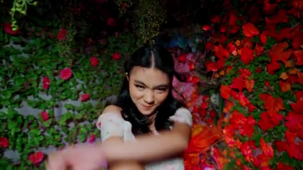 Portret van een vrolijke vrouw omringd door rode bloemen, naar boven kijkend met een dromerige uitdrukking, die 's nachts een gevoel van verwondering en geluk oproept - Video