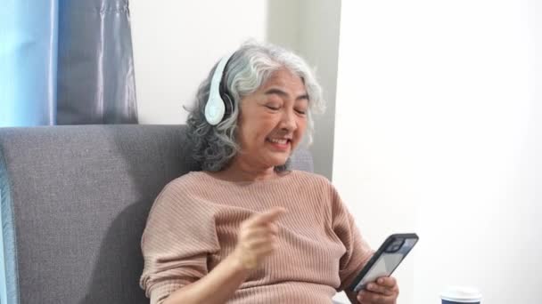 Eine ältere Asiatin nutzt ein Smartphone, um online zu bezahlen. Spiele spielen, soziale Kommunikationsarbeit, soziale Medien spielen, E-Mails checken, auf dem Sofa im Wohnzimmer sitzen. - Filmmaterial, Video