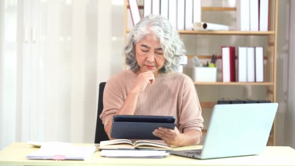 Ältere Asiatin erledigt Papierkram am Computer-Schreibtisch, während sie zu Hause ist Seriöses Gesicht und Stapel von Dokumenten auf dem Tisch, Konzept für die Heimarbeit. - Filmmaterial, Video