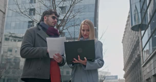 Business entrepreneurs engage in a productive outdoor meeting, analyzing documents and data on a laptop and papers in an urban backdrop. - Footage, Video