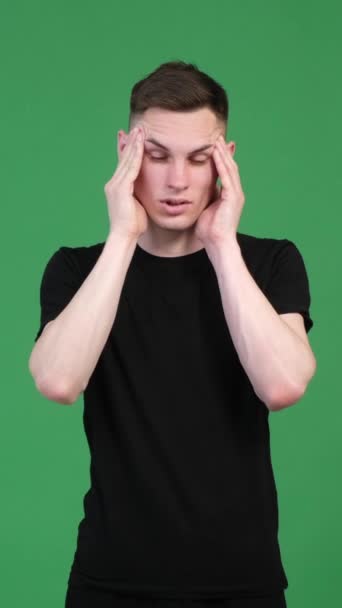 Unhappy Caucasian man suffering from headache on green background. Fatigue, annoyance, melancholy and emotional stress. Vertical video. - Footage, Video