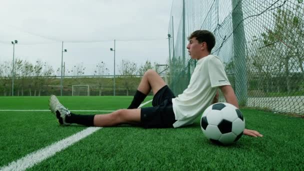 Підлітковий футболіст сидить на боці кидка дихає сильно втомленим - Кадри, відео
