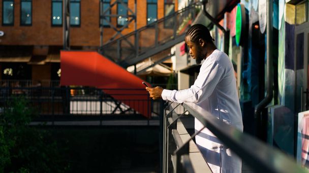 Millenniumi generációs afro-amerikai férfi gépelés sms szabadtéri 5g internet koncepció. Nagy sebességű internet telefonon és csevegés a közösségi oldalakon és blogon - Fotó, kép