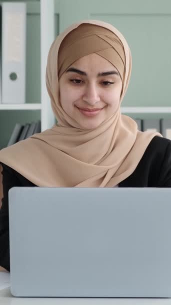 オフィスの休憩中にヒジャーブを着たフレンドリーで陽気なアラビアの女性マネージャー. 笑顔のビジネスマン。 バーティカルビデオ. - 映像、動画