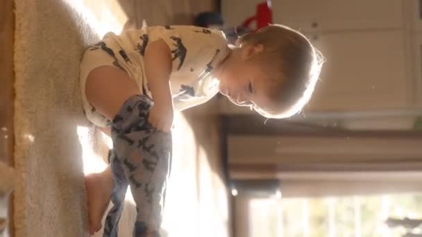 Pikkulapsi istuu lattialla, harjoittaa lelu käärme pitämällä, liikkuvat, ja tutkia sen ominaisuuksia. Pystysuora kuvamateriaali. - Materiaali, video