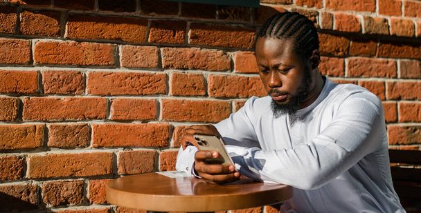 Millennial γενιά Αφροαμερικανός άνθρωπος δακτυλογράφηση sms υπαίθρια 5g έννοια στο διαδίκτυο. Internet υψηλής ταχύτητας στο τηλέφωνο και κουβέντα σε κοινωνικά δίκτυα και blog - Φωτογραφία, εικόνα