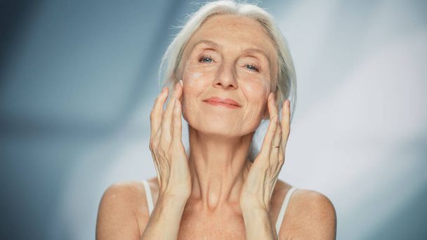 Portrait of Beautiful Senior Woman Gently Applying Face Cream. Elderly Lady Makes Her Skin Soft, Smooth, Wrinkle Free with Natural anti-aging - Fotó, kép