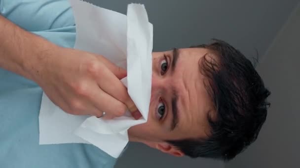 Irritated man sneezes trying to wipe running nose with napkin. Young male person caught cold on autumn day sitting in unheated apartment closeup Vertical footage. - Footage, Video