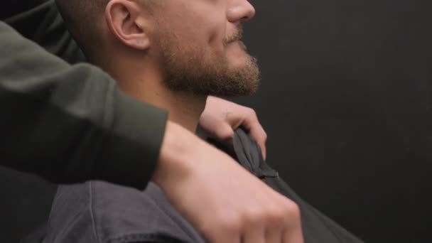 Parturi kattaa hymyilevä mies hartiat viitta valmistautuu leikata hiukset parturissa. Kampaaja palvelee miespuolista asiakasta kauneushoitolassa. Kampaajien työt - Materiaali, video