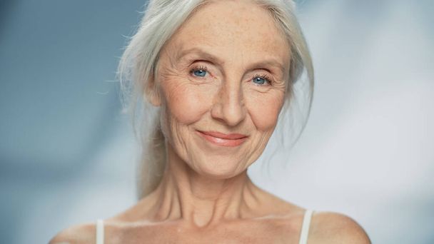 Detailní záběr na portrét krásné starší ženy dívající se na kameru a nádherně se usmívající. Nádherná starší dáma s přírodní svěží šedé vlasy, modré oči - Fotografie, Obrázek