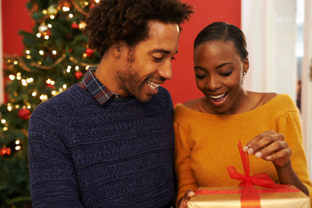 Χριστούγεννα, δώρο και μαύρο ζευγάρι δίνοντας ένα κουτί ή έκπληξη κατά τη διάρκεια γιορτινών διακοπών ή διακοπών με ευτυχία. Ενθουσιασμένοι, γυναίκα και άντρας προσφέρουν ένα δώρο στο σπίτι με αγάπη και καλοσύνη στο γάμο.. - Φωτογραφία, εικόνα