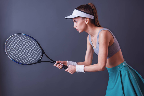 Kaunis tyttö urheiluvaatteet on tilalla tennismaila, harmaalla pohjalla
 - Valokuva, kuva