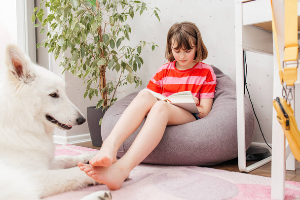 Une adolescente se couche par terre dans sa chambre et lit un livre, à côté d'elle se trouve un chien, un berger suisse blanc. Lire des livres comme passe-temps. - Photo, image