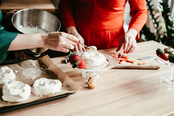 A chef in a teal apron carefully shapes meringues on a baking sheet, surrounded by a lively kitchen setting with fresh fruits like pineapple and oranges adding a splash of color. High quality photo - Photo, Image
