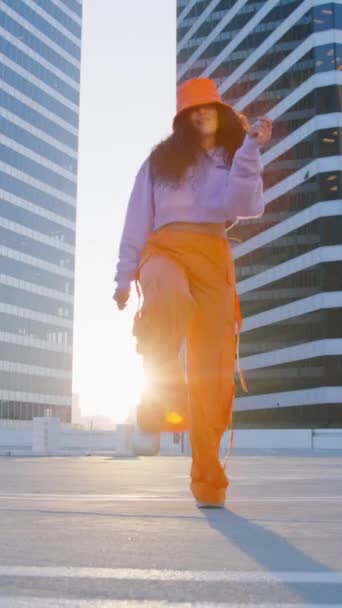 Κάθετο βίντεο. Cool μοντέρνα καλλιτέχνης πόλη street dance performance στην οροφή του ηλιοβασιλέματος. Επιθετική ταλαντούχα γυναίκα μικτής φυλής που χορεύει. Σέξι κορίτσι εκτελεί σύγχρονες κλαμπ προκλητικές κινήσεις του σώματος - Πλάνα, βίντεο
