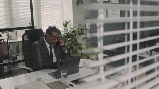 Egy üveg felvételen keresztül, amin tapasztalt biraciális ügyvéd telefonál az ügyféllel, hogy jogi dokumentumokat készítsen az irodában. - Felvétel, videó
