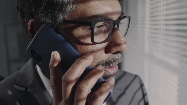 Крупним планом досвідчений бородатий керівник Бірао в окулярах і костюм має телефонну розмову з діловим партнером і обговорення проблем роботи в сучасному офісі - Кадри, відео