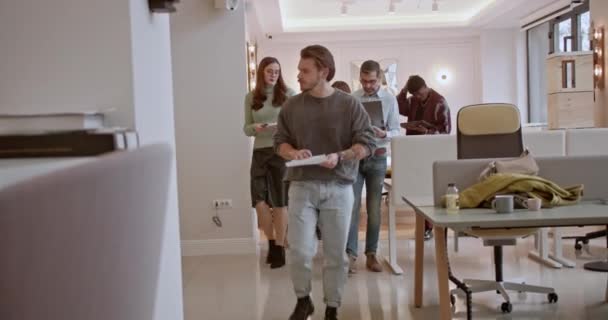 Group of professional entrepreneurs engaged in a discussion while walking in a modern office, carrying documents and a laptop for a business strategy meeting. - Footage, Video