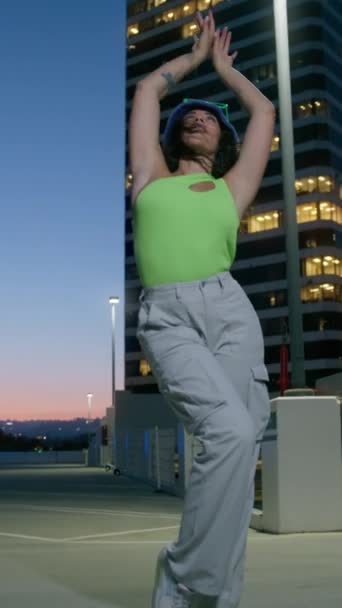 Vertikales Video. Lustige Frau mit langen lockigen Haaren, die auf dem Dachparkplatz tanzt und die Nacht in der Innenstadt genießt. Verrückte flippige Stimmung mit Live-Kamerafahrten, multirassische Tänzer, die lustigen Streetstyle-Tanz aufführen - Filmmaterial, Video