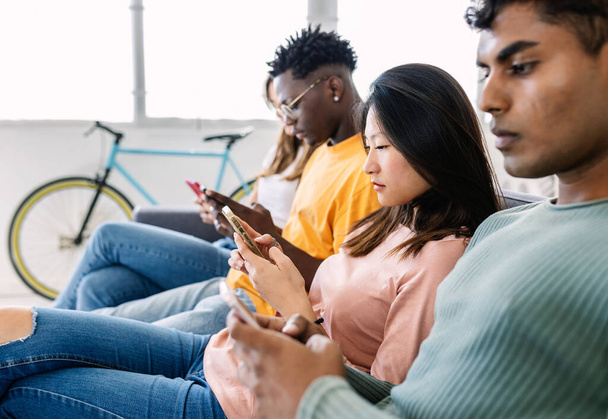 Diverse groep jonge vrienden met behulp van smartphone op de bank thuis. Technologie en socialmediaverslaving - Foto, afbeelding