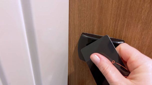 Close-up άποψη ενός επισκέπτη χέρι χρησιμοποιώντας μια μαύρη κάρτα-κλειδί για να ξεκλειδώσετε μια πόρτα δωματίου ξενοδοχείου, αποδεικνύοντας την ασφάλεια και την ευκολία των σύγχρονων συστημάτων πρόσβασης στο ξενοδοχείο. - Φωτογραφία, εικόνα