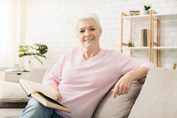 Sorrindo mulher idosa relaxante com livro em casa, espaço livre
 - Foto, Imagem