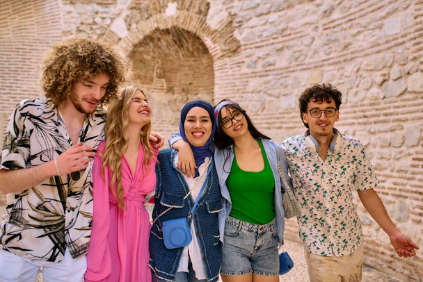 Een gevarieerde groep toeristen, gekleed in zomerkleding, slentert door de toeristische stad met brede glimlachen, genietend van hun sightseeing avontuur.  - Foto, afbeelding
