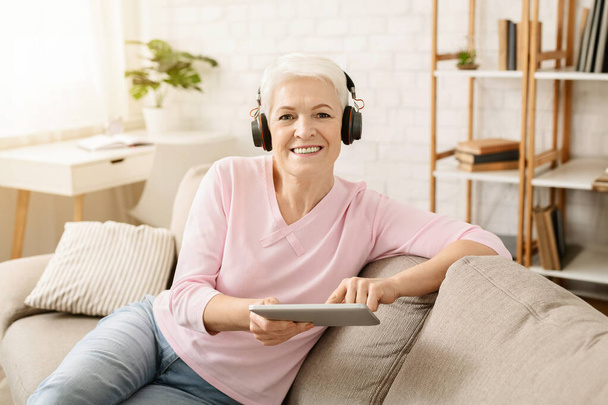 Seniorin genießt Musik und Videos auf Tablet-PC über Kopfhörer, freier Platz - Foto, Bild