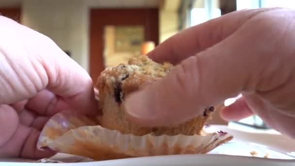 Egy férfi keze kinyitja az áfonyás muffint egy tányéron a muffin formájából..   - Felvétel, videó